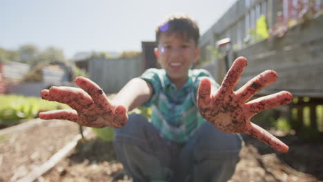 Portrait-of-happy-biracial-boy-showing-hands-covered-in-dirt,-slow-motion,-copy-space