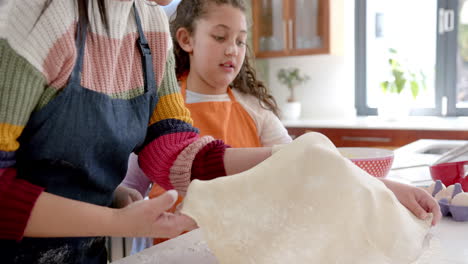 Happy-biracial-mother-and-daughter-taking-care-of-dough-in-sunny-kitchen