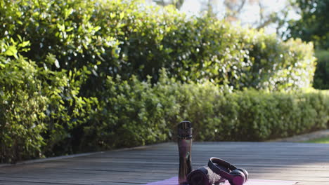 Water-bottle,-headphones,-towel-and-yoga-mat-on-deck-in-sunny-garden,-copy-space,-slow-motion