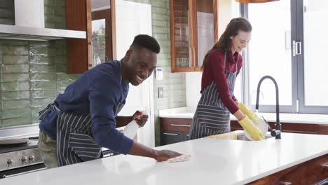 Happy-diverse-couple-washing-dishes-and-cleaning-top-in-kitchen,slow-motion