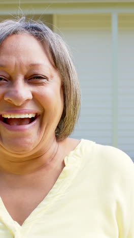 Vídeo-Vertical-De-Retrato-De-Una-Feliz-Mujer-Birracial-Mayor-Sonriendo-Fuera-De-Casa,-Cámara-Lenta