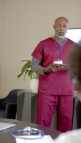 Vertical-video-of-african-american-male-doctor-talking-by-tablet-with-copy-space,-slow-motion