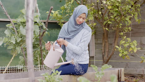 Glückliche-Biracial-Frau-In-Hijab,-Die-Pflanzen-Gießt,-Gartenarbeit-Mit-Kopierraum,-Zeitlupe