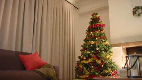 Christmas-tree-by-fireplace-in-living-room-with-closed-curtains-at-home,-copy-space,-slow-motion