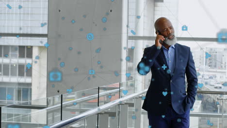 Animation-of-connected-icons-over-african-american-businessman-walking-while-talking-on-cellphone