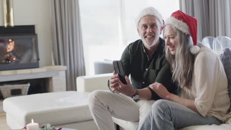Middle-aged-caucasian-couple-in-santa-hats-on-tablet-video-chat-at-christmas-at-home,-slow-motion