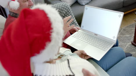 Senior-caucasian-couple-in-santa-hats-with-laptop-with-copy-space-at-christmas,-slow-motion
