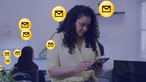 Animation-of-envelope-icon-in-circles-over-biracial-woman-scrolling-on-digital-tablet-in-office