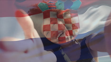 Animation-of-flag-of-croatia-waving-over-biracial-woman-talking-selfie-video-with-camera-at-beach