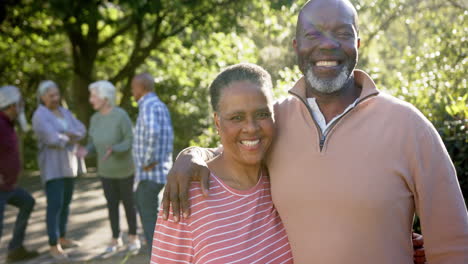 Portrait-of-happy-african-american-senior-couple-embracing-in-sunny-garden-with-friends,-slow-motion