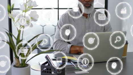 Animation-of-multiple-icons-over-african-american-man-working-on-laptop-in-office