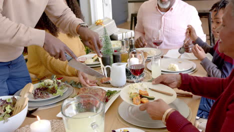 African-american-father-carving-meat-at-multi-generation-family-dinner-table