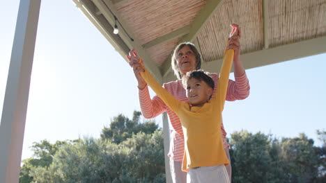 Glückliche-ältere-Großmutter-Mit-Gemischter-Abstammung-Und-Ihr-Enkel-Machen-Yoga,-Meditieren-Auf-Der-Terrasse,-Zeitlupe