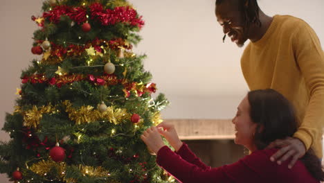 Happy-diverse-couple-decorating-christmas-tree-at-home,-slow-motion