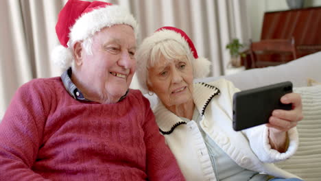 Älteres-Kaukasisches-Paar-Mit-Weihnachtsmützen,-Das-Sein-Smartphone-Für-Einen-Weihnachtsvideoanruf-In-Zeitlupe-Nutzt