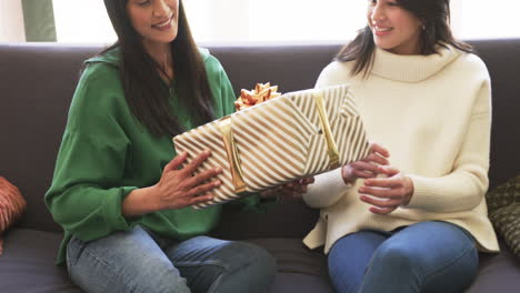 Happy-biracial-mother-and-adult-daughter-exchanging-christmas-gift-at-home,-slow-motion