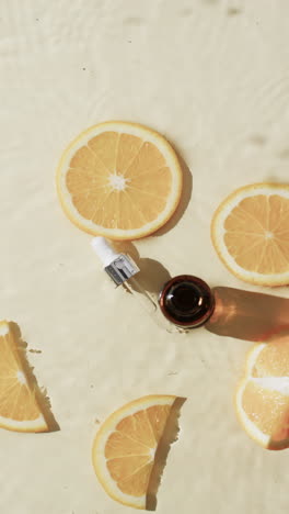 Vertical-video-of-beauty-product-bottle,-orange-slices-in-water-with-copy-space-on-yellow-background