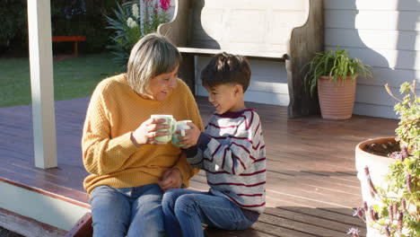 Glückliche-ältere-Großmutter-Und-Enkel-Mit-Gemischter-Abstammung,-Die-Tassen-Auf-Der-Terrasse-Halten,-Zeitlupe