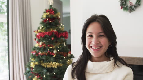 Portrait-of-happy-biracial-woman-smiling-by-christmas-tree-at-home,-copy-space,-slow-motion