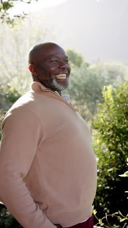 Retrato-En-Video-Vertical-De-Un-Feliz-Hombre-Afroamericano-Mayor-Sonriendo-En-La-Naturaleza-Soleada,-Cámara-Lenta