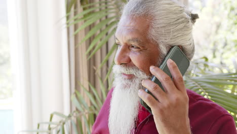 Happy-biracial-senior-man-with-white-beard-on-smartphone-in-sunny-room,-copy-space,-slow-motion