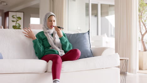 Mujer-Birracial-En-Hijab-Usando-Un-Teléfono-Inteligente-En-Un-Sofá-En-Casa-Con-Espacio-Para-Copiar,-Cámara-Lenta