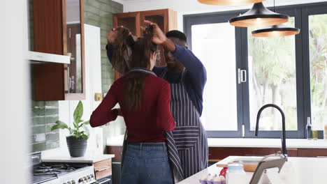 Happy-diverse-couple-wearing-aprons-in-kitchen-and-using-tablet,slow-motion