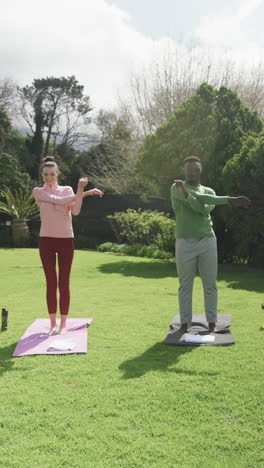 Happy-diverse-couple-exercising-yoga-in-sunny-garden,-slow-motion,-copy-space