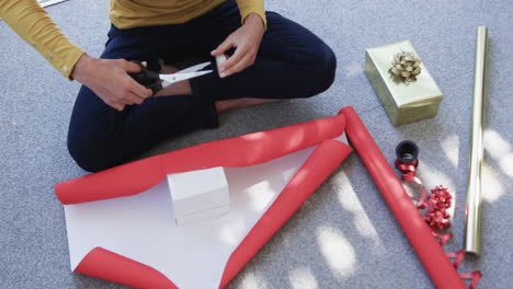 Midsection-of-biracial-woman-sitting-on-floor-packing-christmas-presents,-slow-motion