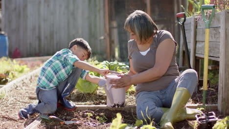 Happy-senior-biracial-grandmother-and-grandson-watering-plants-in-sunny-garden,-slow-motion