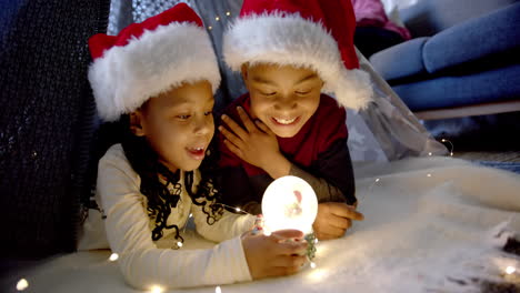 Glücklicher-Afroamerikanischer-Bruder-Und-Schwester-In-Weihnachtsmützen-Spielen-Mit-Schneekugel,-Zeitlupe