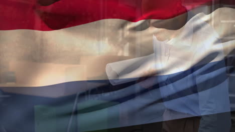 Animation-Der-Niederländischen-Flagge-über-Einem-Biracial-Ingenieur-Mit-Blaupausen,-Der-Den-Grundriss-Inspiziert