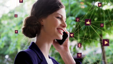 Animation-of-connected-icons-forming-globes-over-smiling-caucasian-woman-talking-on-cellphone