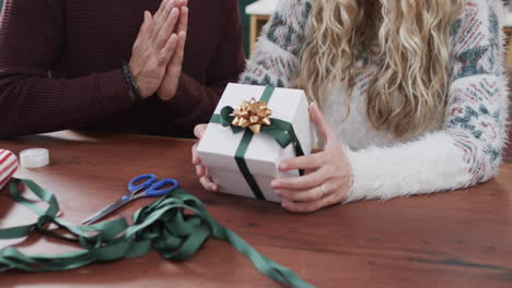 Midsection-of-diverse-couple-sitting-at-table-packing-christmas-presents-at-home,-in-slow-motion