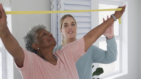 Caucasian-nurse-with-senior-woman-exercising-with-rubber-band,-copy-space,-slow-motion