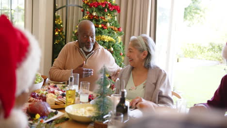 Happy-diverse-senior-couple-talking-at-christmas-dinner-table-with-friends,-slow-motion