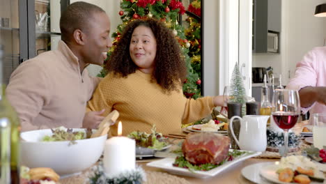 Happy-african-american-couple-talking-and-embracing-at-family-christmas-dinner-table