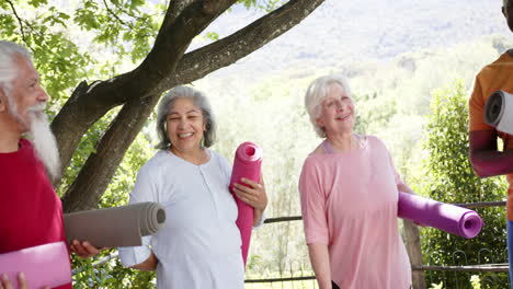 Happy-diverse-senior-male-and-female-friends-holding-yoga-mats-talking-in-sunny-nature,-slow-motion