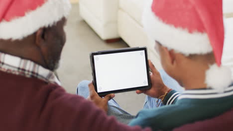 Happy-african-american-father-and-adult-son-in-christmas-hats-using-tablet,-copy-space,-slow-motion