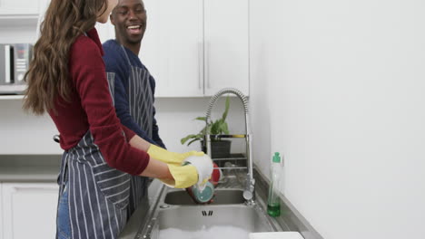 Happy-diverse-couple-washing-dishes,talking-and-laughing-in-kitchen,slow-motion