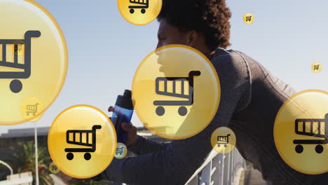 Animation-of-shopping-cart-icons,-tired-african-american-runner-taking-break-and-drinking-water