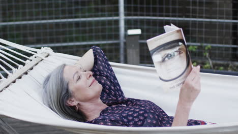Caucasian-middle-aged-woman-reading-book-relaxing-in-hammock-on-terrace-in-nature,-slow-motion