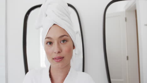 Portrait-of-happy-biracial-woman-wearing-towel-on-head-in-bathroom,-slow-motion,-copy-space