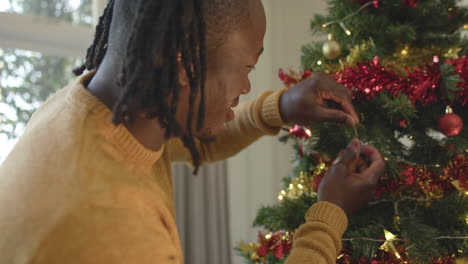 Glücklicher-Afroamerikanischer-Mann-Mit-Dreadlocks,-Der-Den-Weihnachtsbaum-Schmückt,-Zeitlupe