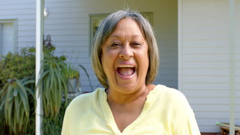 Retrato-De-Una-Feliz-Mujer-Birracial-Mayor-Mirando-La-Cámara-Y-Sonriendo-Fuera-De-La-Casa,-Cámara-Lenta