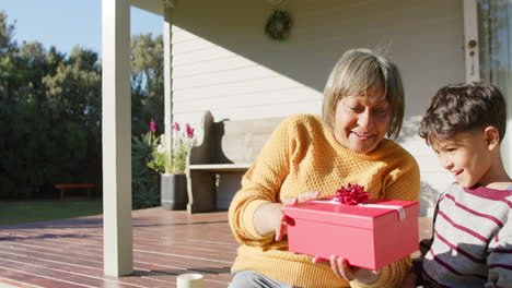 Glückliche-ältere-Großmutter-Und-Enkel-Mit-Gemischter-Abstammung,-Die-Geschenke-Auf-Der-Terrasse-Verteilen,-Zeitlupe,-Kopierraum