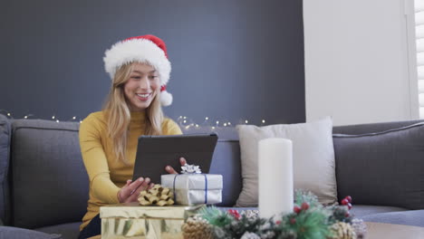 Happy-biracial-woman-wearing-santa-hat-using-tablet-for-christmas-video-call,-in-slow-motion