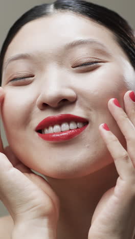 Video-Vertical-De-Una-Mujer-Asiática-Con-Cabello-Negro-Y-Maquillaje-Tocando-La-Cara,-Espacio-Para-Copiar,-Cámara-Lenta