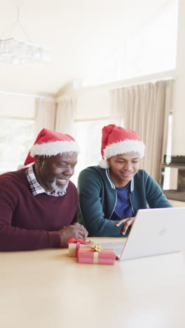 Vertical-video-of-african-american-father-and-son-having-christmas-laptop-video-call,-slow-motion