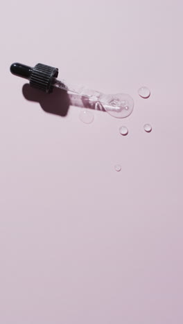 Vertical-video-of-make-up-pipette-and-drops-of-serum-with-copy-space-on-pink-background